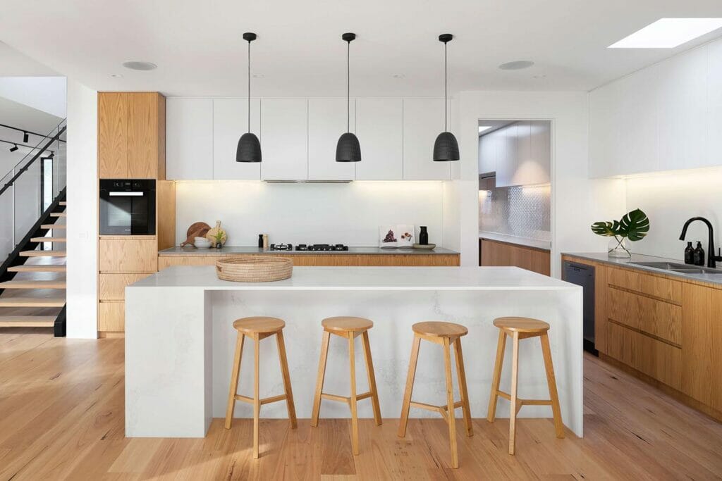 A modern home’s kitchen with a white island, wooden cabinetry, and wood stools.
